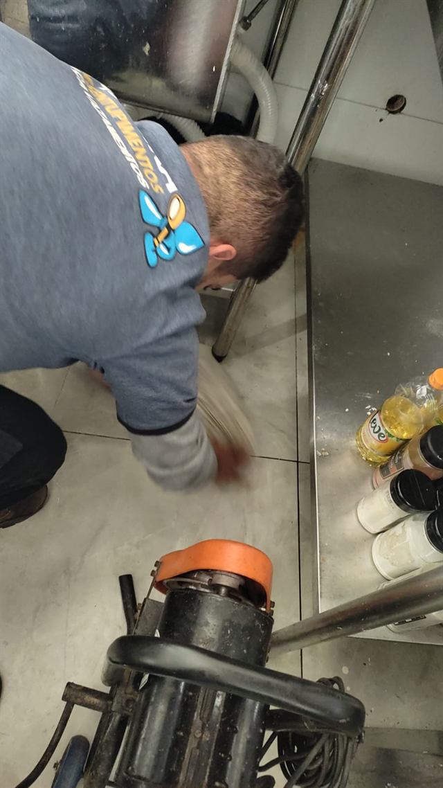Técnico desentupindo o ralo de uma cozinha industrial com máquina rotativa